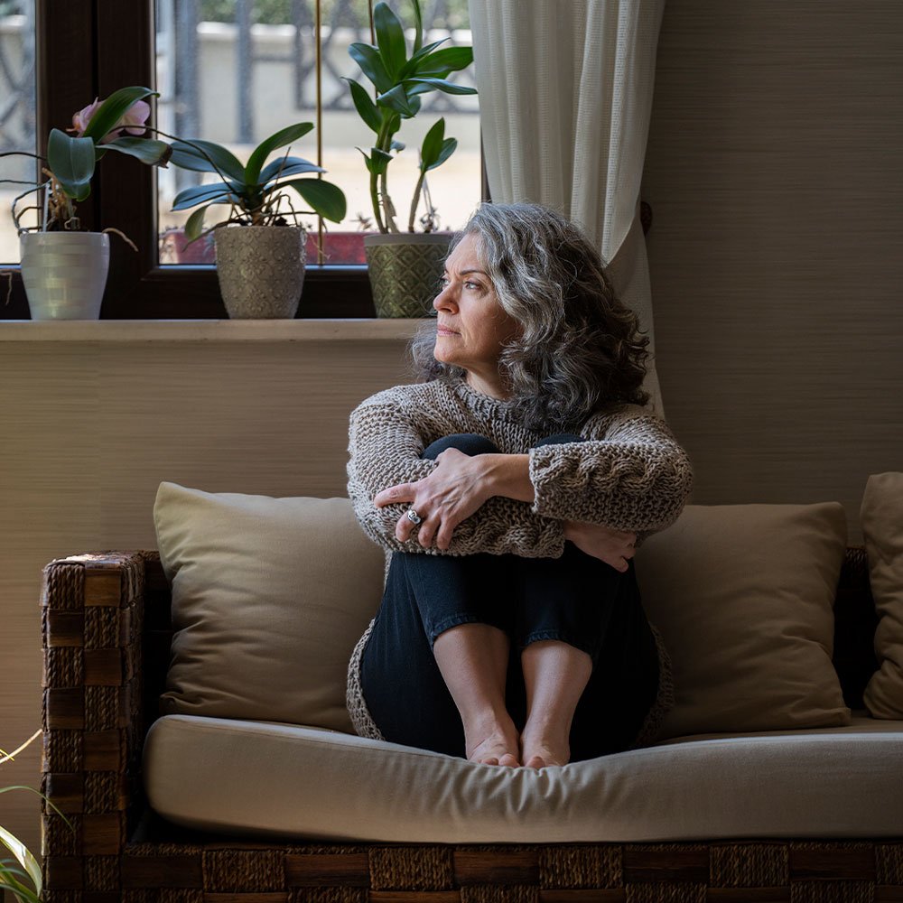 Mulher madura olhando pela janela com expressão tranquila, representando alívio após tratamento da menopausa com endocrinologista em Aracaju.